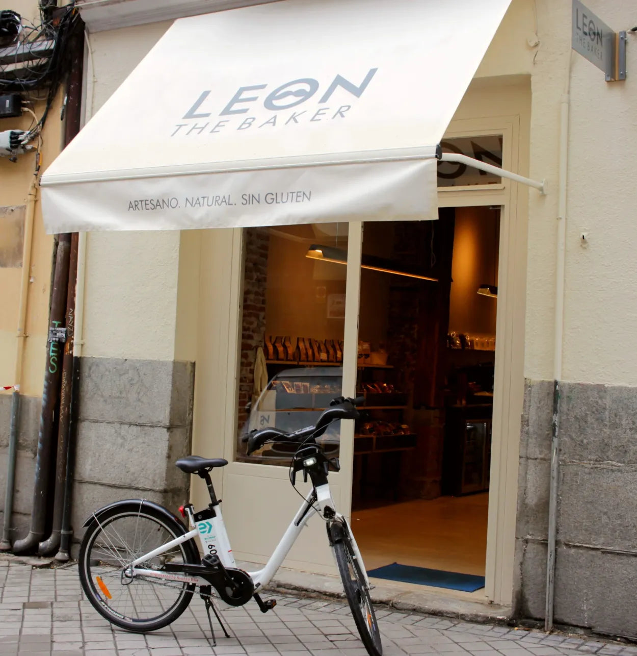 Fachada de una panadería con toldo blanco y escaparate iluminado
